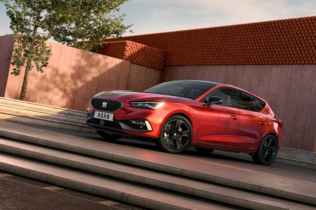 Roter SEAT Leon FR Black Edition steht seitlich auf einer Treppe vor einer Wand mit roten Ziegeln und einem Baum im Hintergrund