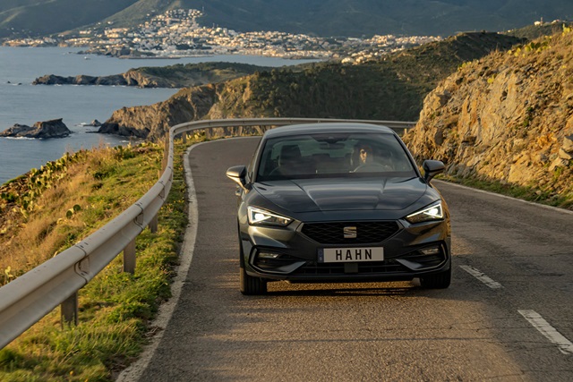 SEAT Leon in Grau fährt auf einer Küstenstraße mit Felsklippen und Meer im Hintergrund