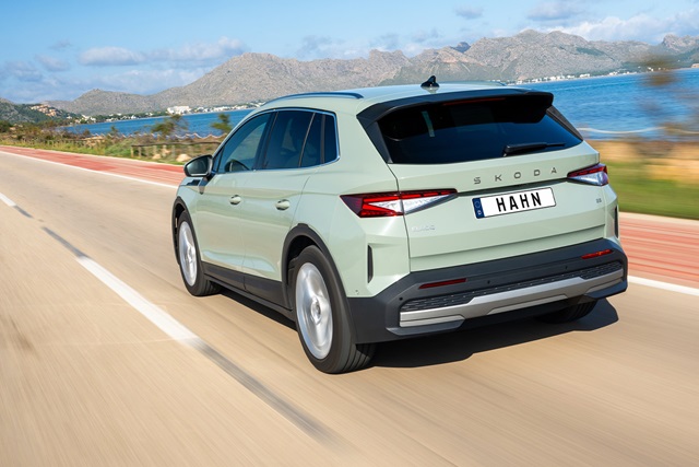 Skoda Elroq in Grün von hinten auf einer Küstenstraße mit Bergen und Meer im Hintergrund