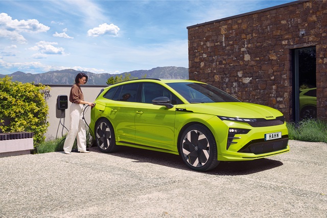 Grüner Skoda Enyaq RS in der Seitenansicht beim Laden steht vor einem roten Backsteingebäude und eine Person ist links vom Fahrzeug