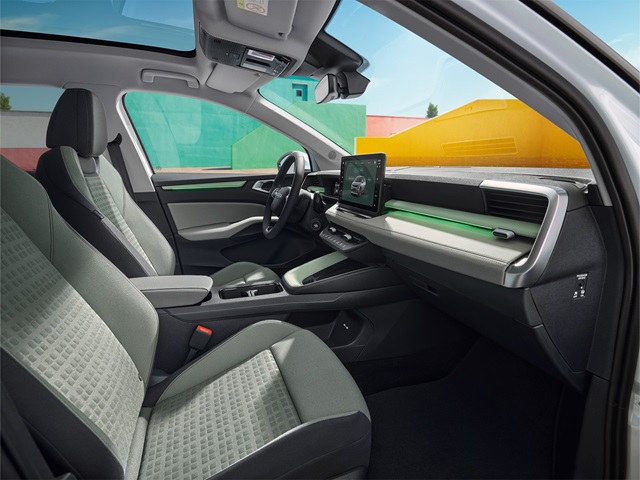 Innenraum eines Fahrzeugs mit zwei Vordersitzen, einem Lenkrad, einem mittig angebrachten Touchscreen und einem Panoramadach