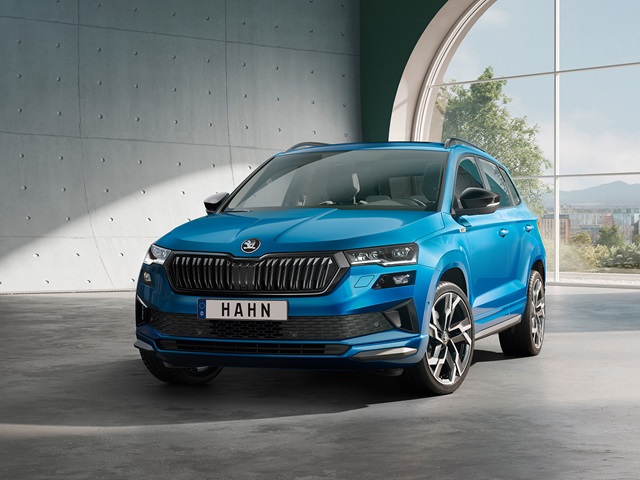 Blauer Škoda Karoq Sportline mit markanter Front und großen Felgen in einem modernen Raum mit Fenster