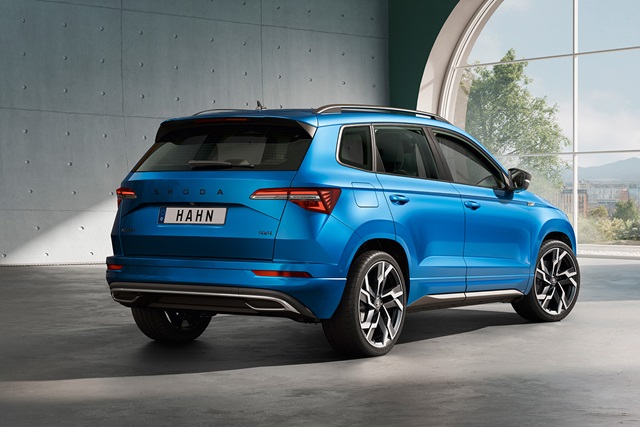 Škoda Karoq Sportline in Blau aus schräger Rückansicht mit großem Schriftzug 'HAHN' auf dem Kennzeichen in heller Halle.