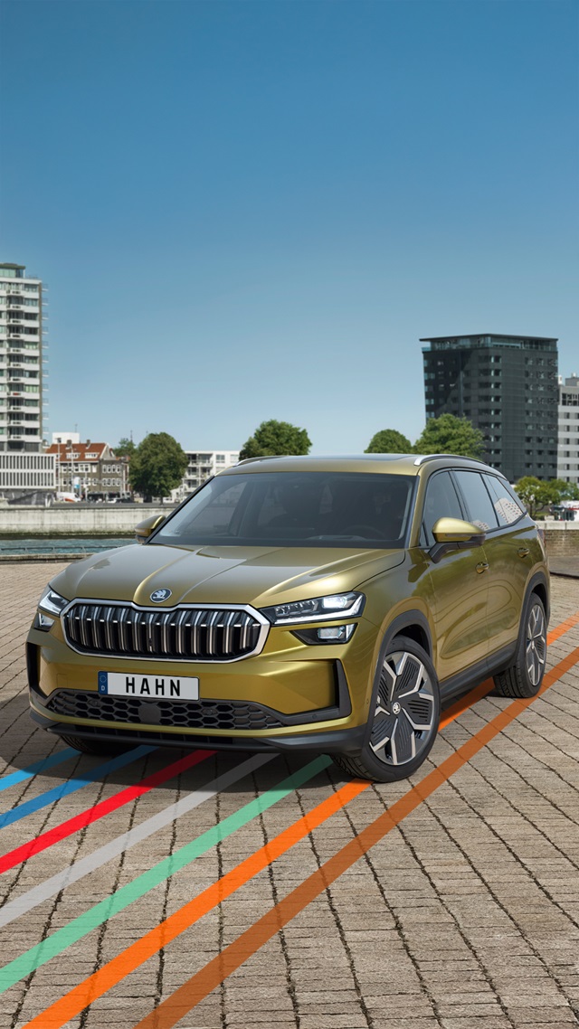 Škoda Kodiaq SUV in gelber Lackierung frontal auf gepflastertem Parkplatz mit mehrfarbigen Linien und städtischer Kulisse im Hintergrund