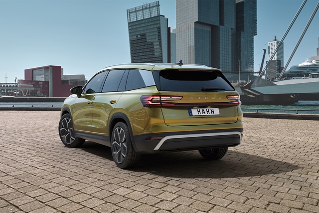 Gelber Škoda Kodiaq Selection von hinten mit getönten Scheiben und markanten Rückleuchten auf gepflastertem Platz vor moderner Stadtarchitektur