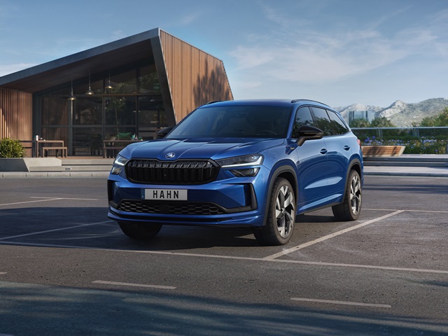 Blauer Škoda Kodiaq Sportline in Frontansicht auf einem Parkplatz vor modernem Gebäude mit Bergkulisse