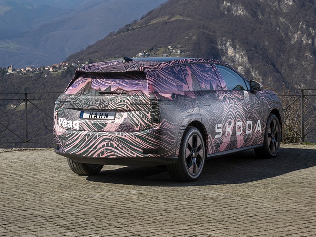 Heckansicht eines Škoda Peaq Erlkönigs mit auffälliger Camouflage-Folie und großem Škoda-Schriftzug auf der Seite vor Bergkulisse