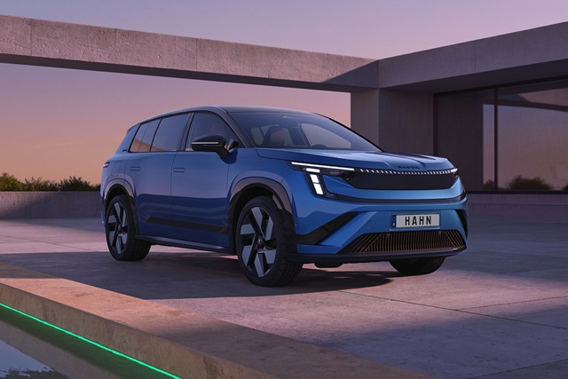 Blauer Škoda Peaq Sportline in Frontansicht auf modernem Betonpodest bei Dämmerung mit reflektierendem Glasgebäude im Hintergrund