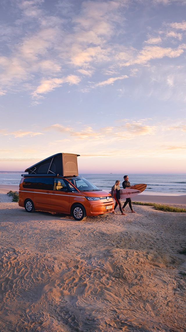 Der Volkswagen California Beach an der Küste mit zwei Surfern.