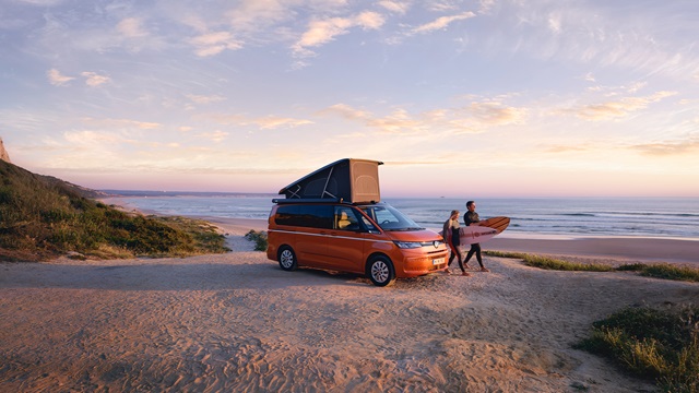Der Volkswagen California Beach an der Küste mit zwei Surfern.
