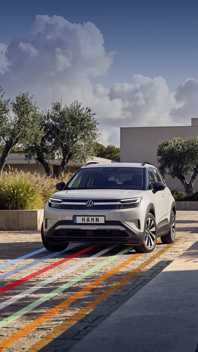 VW ID. Cross Life in Grau von vorne auf gepflastertem Platz mit Bäumen und modernem Gebäude im Hintergrund