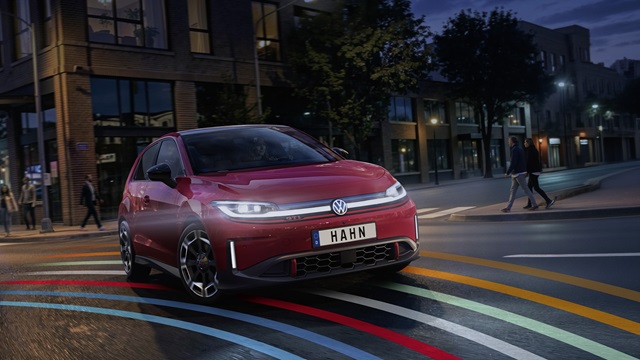 VW ID. Polo GTI in roter Lackierung mit LED-Scheinwerfern und markanten Felgen in Frontansicht auf einer Straße mit bunten Linien, Kennzeichen 'HAHN'