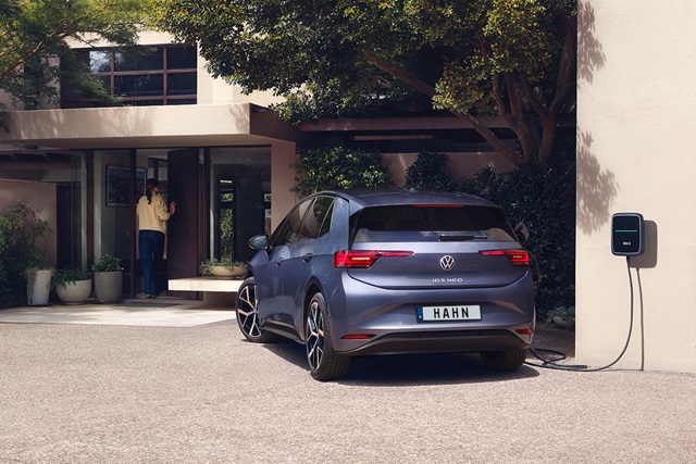 Blauer VW ID.3 Neo steht rückseitig an einer Hauswand und ist an eine Ladestation angeschlossen