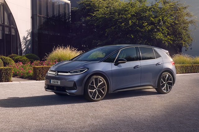 Seitliche Ansicht eines blauen VW ID.3 Neo vor einem modernen Gebäude mit Büschen und Bäumen im Hintergrund