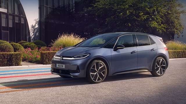 Seitliche Ansicht eines blauen VW ID.3 Neo mit markanten Felgen vor einem modernen Gebäude und Büschen