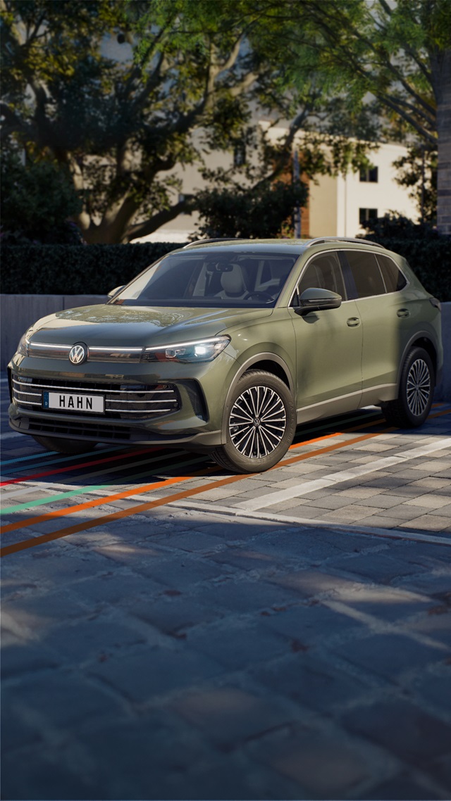 VW Tiguan Elegance in grün in Frontansicht auf gepflastertem Parkplatz mit Bäumen und Gebäuden im Hintergrund
