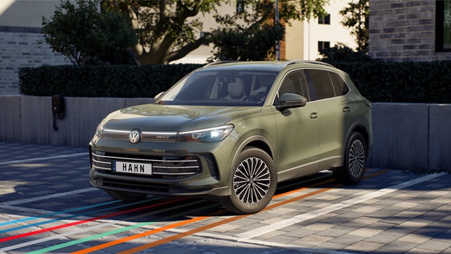 VW Tiguan Elegance in grün in Frontansicht auf gepflastertem Parkplatz mit Bäumen und Gebäuden im Hintergrund