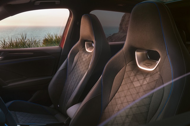 Innenraum des VW Tiguan mit zwei Sportsitzen, die ein R-Logo und eine diamantförmige Steppung aufweisen, vor einer Landschaft mit Meer und Felsen im Hintergrund