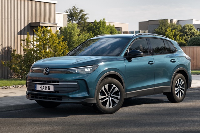 Blauer VW Tiguan Life in Seitenansicht vor modernen Wohnhäusern mit schwarzem Dachgepäckträger und markanten Felgen
