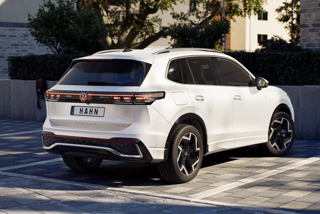 Weiße VW Tiguan R-Line SUV-Heckansicht mit getönten Scheiben, markanten Rückleuchten und Dachspoiler auf gepflastertem Platz vor Gebäuden