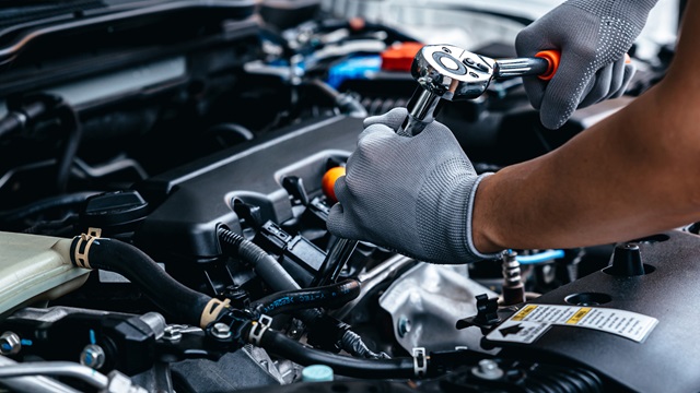 Hände mit schwarzen Handschuhen bedienen einen Schraubenschlüssel an einem Motor in einer Werkstatt